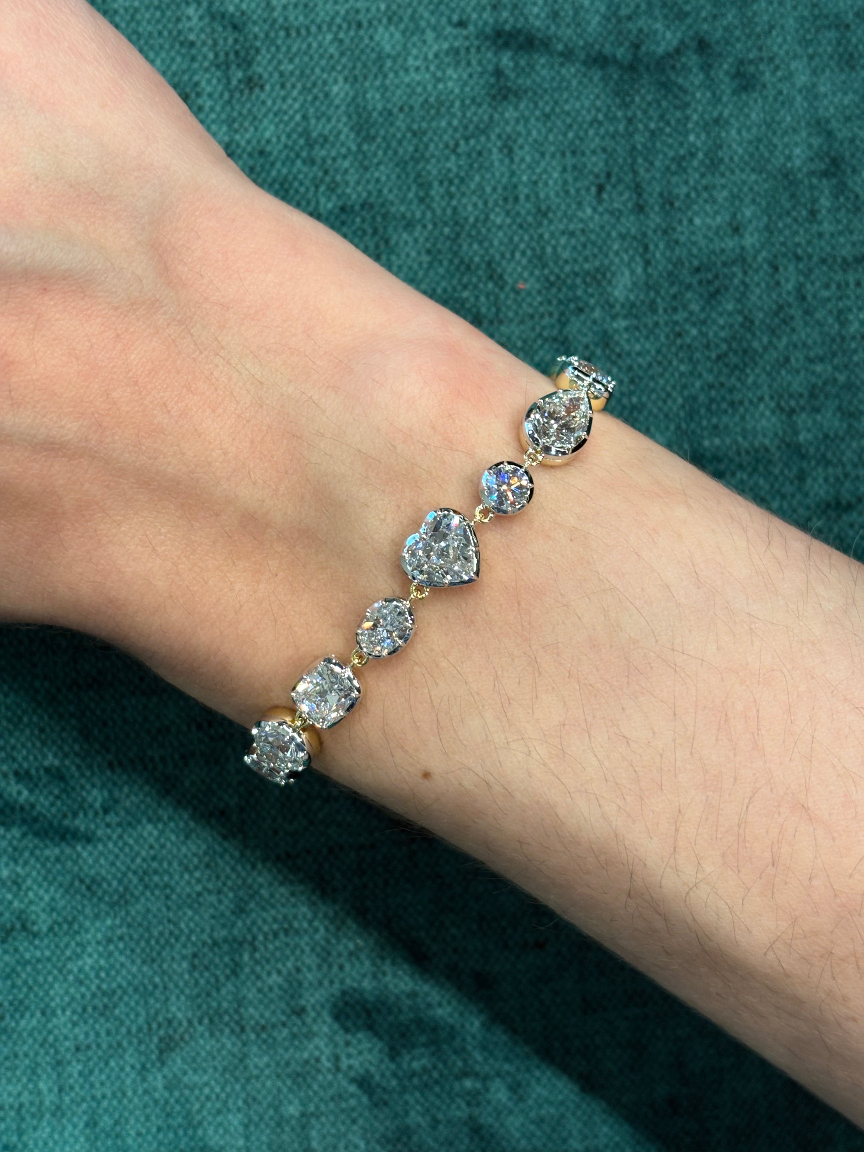 A close-up of a wrist wearing the Mixed Shape Collet Set Diamond Tennis Bracelet in white gold, featuring seven large diamonds totaling 13.38 ctw, displayed against a teal fabric background.