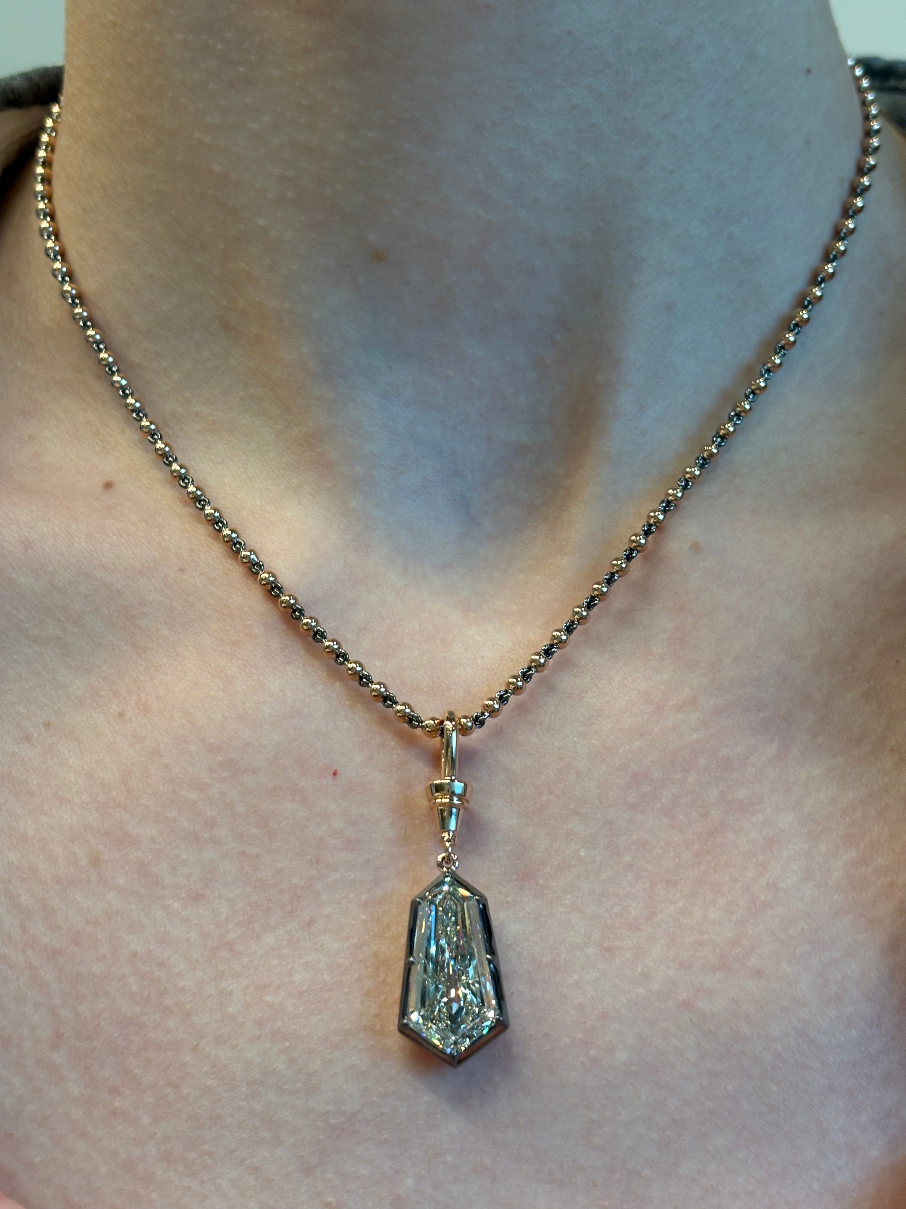 A close-up of a person wearing the Collet Set Shield Cut Diamond Necklace in Yellow Gold and Black Rhodium—a striking piece featuring a large, geometric diamond pendant—resting elegantly at the base of their neck.