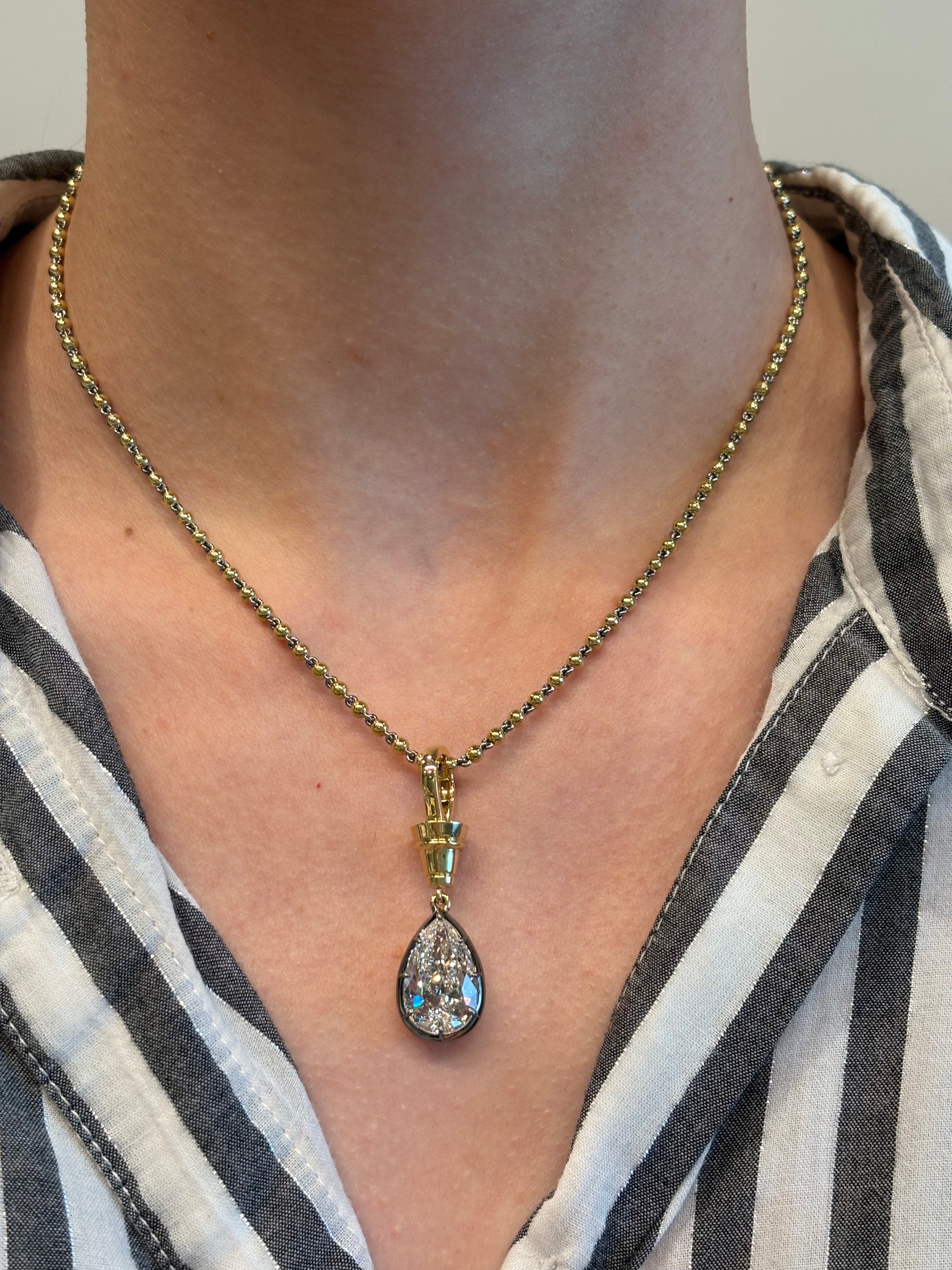 A person with a light skin tone, dressed in a black-and-white striped shirt, wears the Collet Set Pear Shape Diamond Necklace in Black Rhodium and Yellow Gold featuring a sparkling 5.19ctw teardrop pendant.