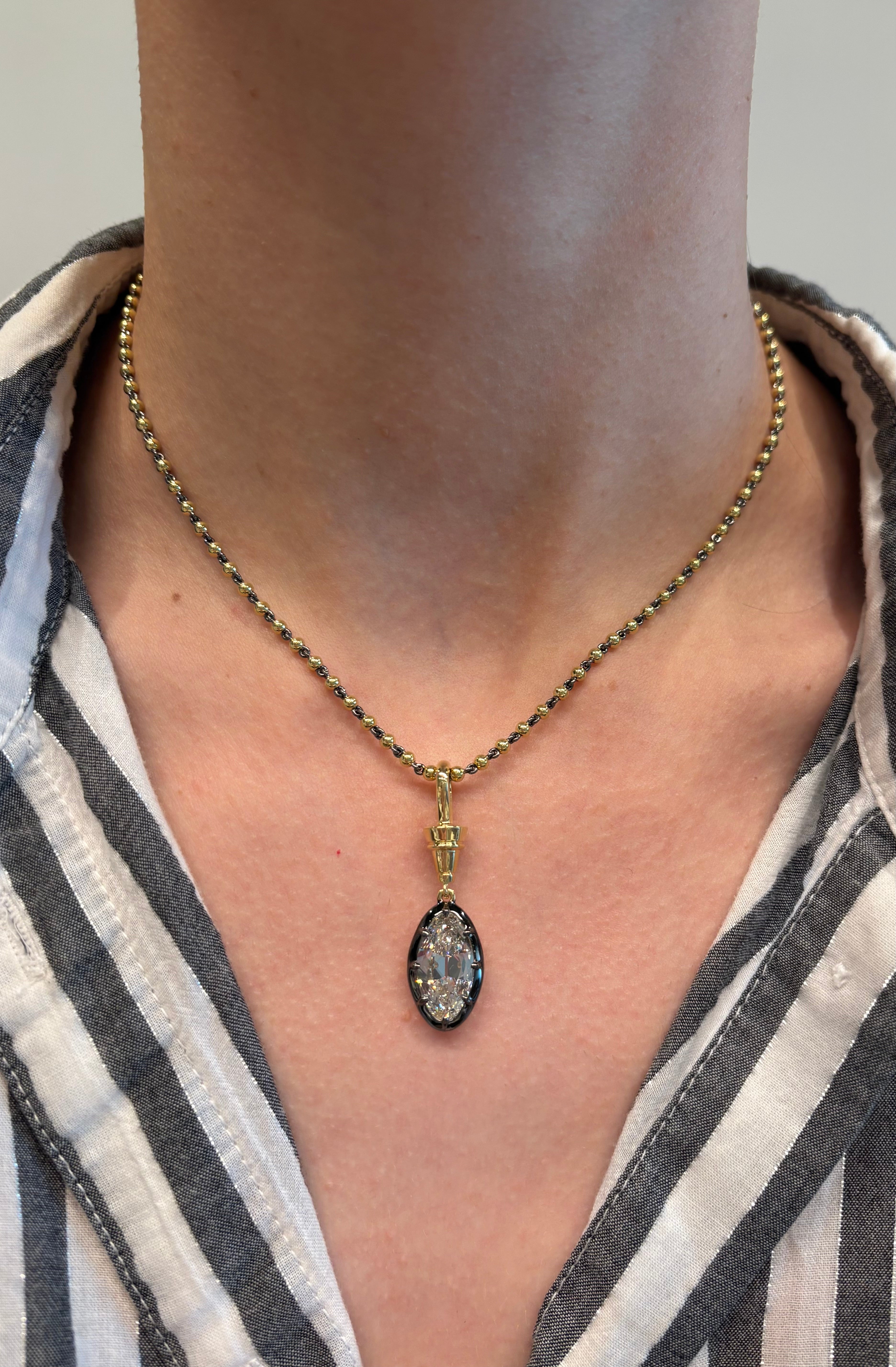 A close-up of a person wearing the Collet Set Old Mine Diamond Necklace in Yellow Gold and Black Rhodium, featuring an oval-shaped 4.04ctw diamond pendant with beaded detailing, against skin and a striped button-up shirt.