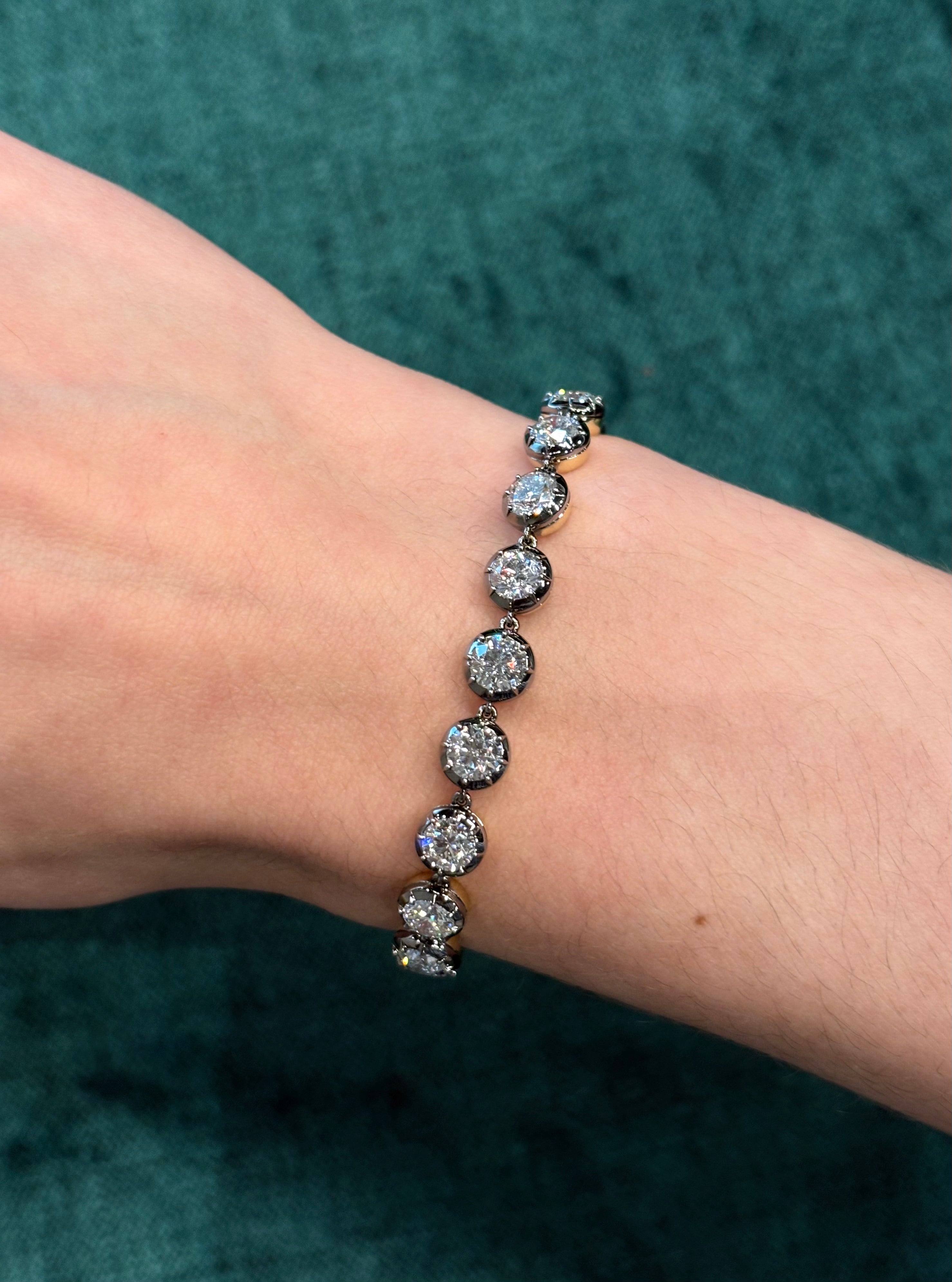 A hand wearing the Collet Set Round Diamond Tennis Bracelet in Black Rhodium, featuring large round diamonds totaling 9.02 ctw, is shown against a textured teal background.