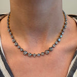 A close-up of a neck wearing the Collet Set Graduating Round Diamond Necklace in Black Rhodium, featuring round diamonds totaling 19.10ctw in a single strand, paired with a striped shirt and v-shaped neckline.
