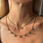 A close-up of a woman's neck wearing two Bezel Set Heart Shape Diamond Station Necklaces with Ball Chains in yellow gold, the heart-shaped pendants reflecting sunlight on her skin.