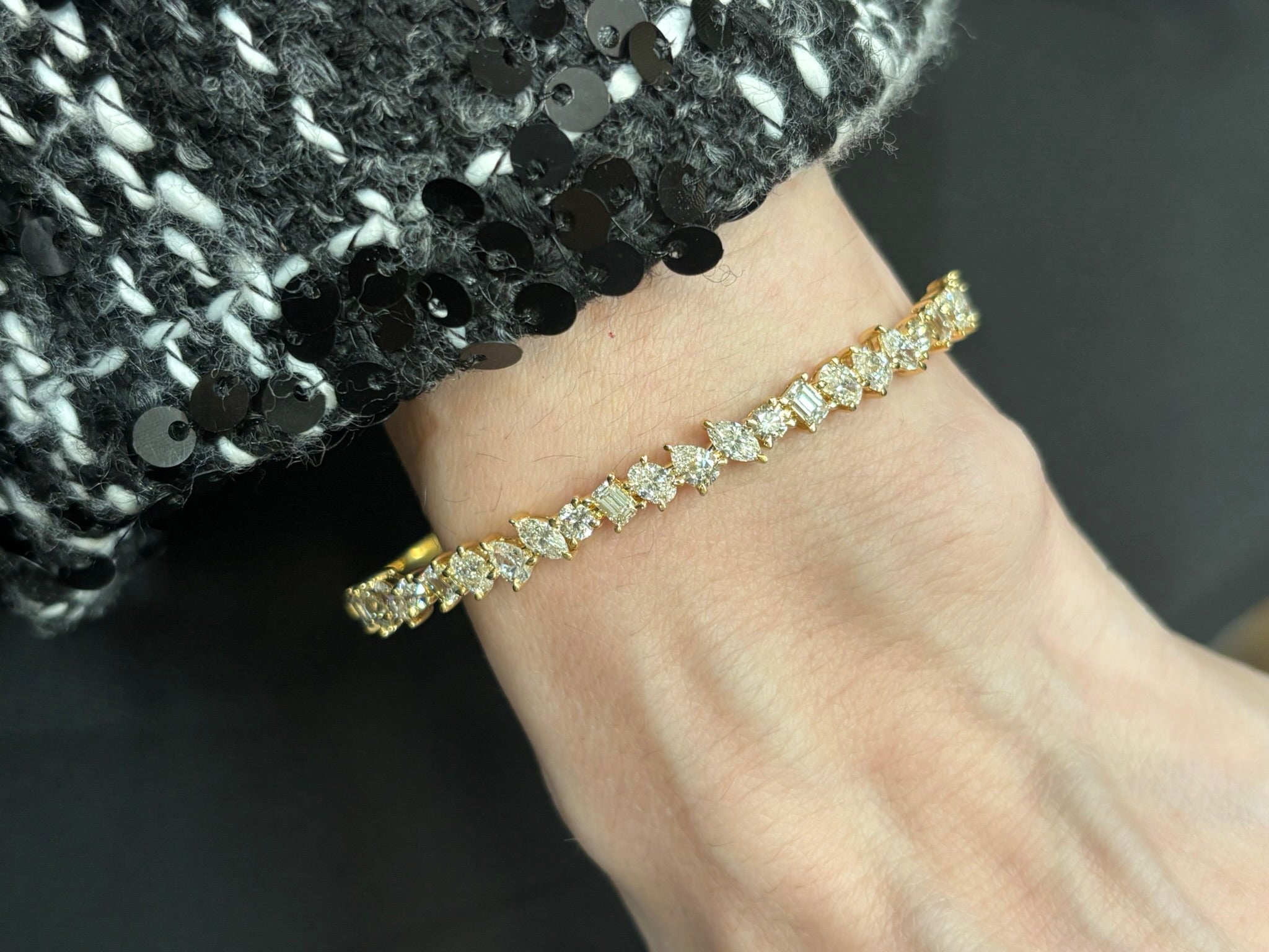 A close-up of a wrist wearing the Marching Mixed Shape Diamond Bangle in 18K rose gold, set with sparkling stones, paired with a black and white sequined sleeve.