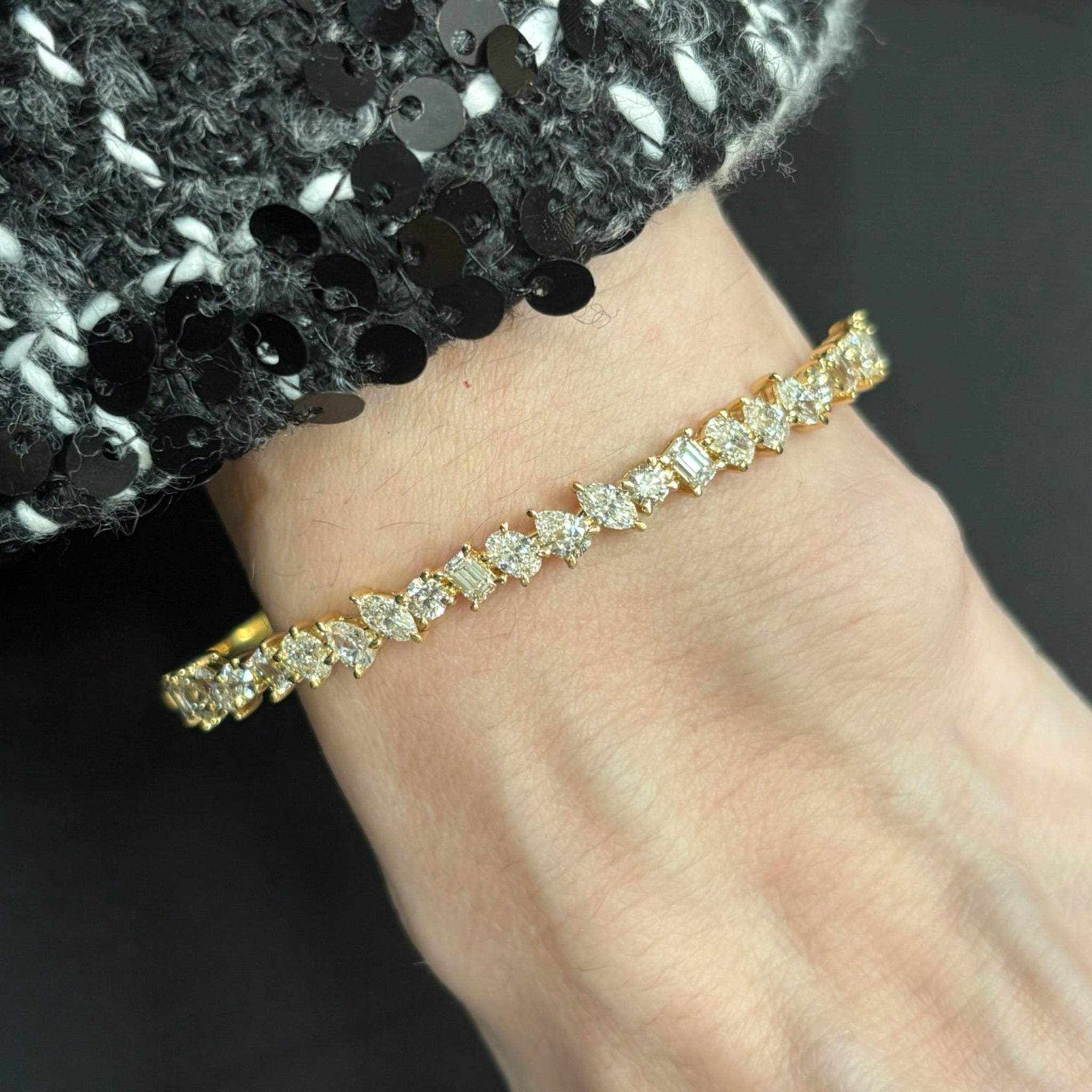 A close-up of a wrist wearing the Marching Mixed Shape Diamond Bangle in 18K rose gold, set with sparkling stones, paired with a black and white sequined sleeve.