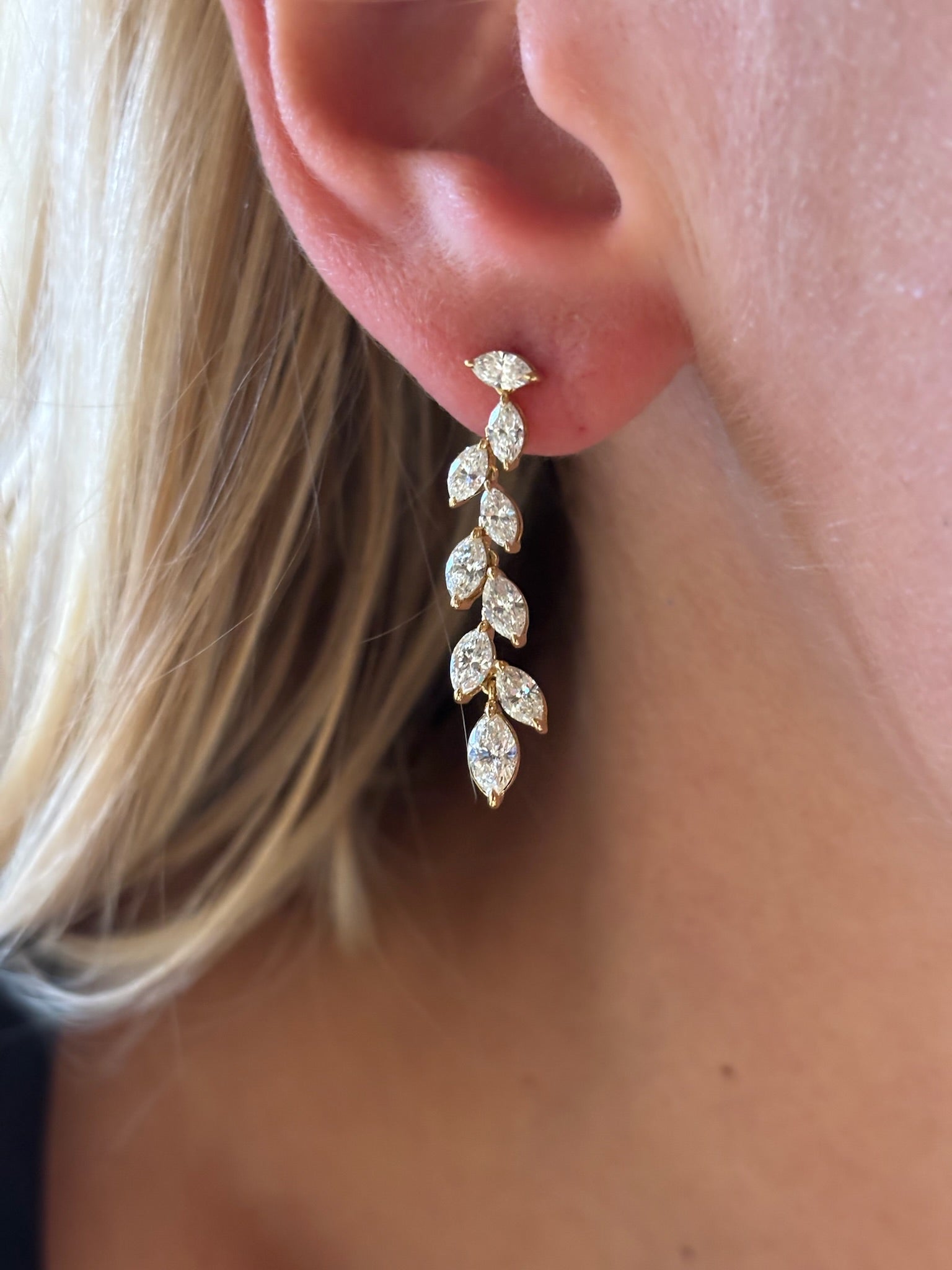 A close-up of a woman's ear wearing Marquise Diamond Waterfall Drop Earrings in Yellow Gold, featuring seven marquise, leaf-like diamond segments cascading elegantly.