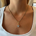 A close-up of a woman wearing the Collet Set Heart Shape Diamond Necklace in Black Rhodium and Yellow Gold against her bare neck and a white ribbed shirt.