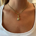 A close-up of a person wearing the Collet Set Cushion Cut Yellow Diamond Necklace in Black Rhodium and Yellow Gold with a white scoop-neck top, highlighting the jewelry and collarbone area.