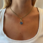 A woman wears a white top and the Collet Set Heart Shape Blue Sapphire Necklace in Black Rhodium and Yellow Gold, with focus on her neck and collarbone.
