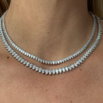 A close-up of a woman's neck wearing two layered necklaces: the upper is the Pear Diamond Tennis Necklace in White Gold, while the lower features larger marquise-shaped diamonds.