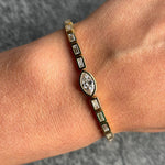 A close-up of a wrist wearing the East-West Bezel Set Marquise and Baguette Diamond Tennis Bracelet in Yellow Gold, set against a textured gray background.