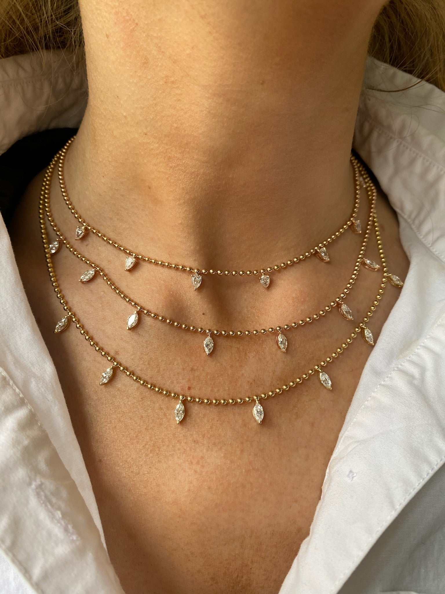 A close-up of a person wearing three layered Spike Ball Chain Necklaces with marquise diamonds, paired with a white collared shirt.