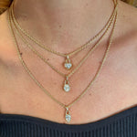 A close-up of a person wearing the Collet Set Locket Motif Diamond Pendant Necklace in layered yellow or white gold, each with unique diamond motifs, over bare skin and a black, strapless, ribbed top.