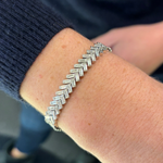 A close-up of a wrist wearing the Half-Bezel Set Chevron Diamond Tennis Bracelet in White Gold, medium size, with a zigzag pattern of clear diamonds. The person wears a dark, ribbed sleeve.