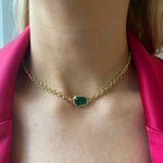 A woman wears the Chain Necklace in Yellow Gold with an Emerald Cut Emerald, styled with a bright pink blazer.