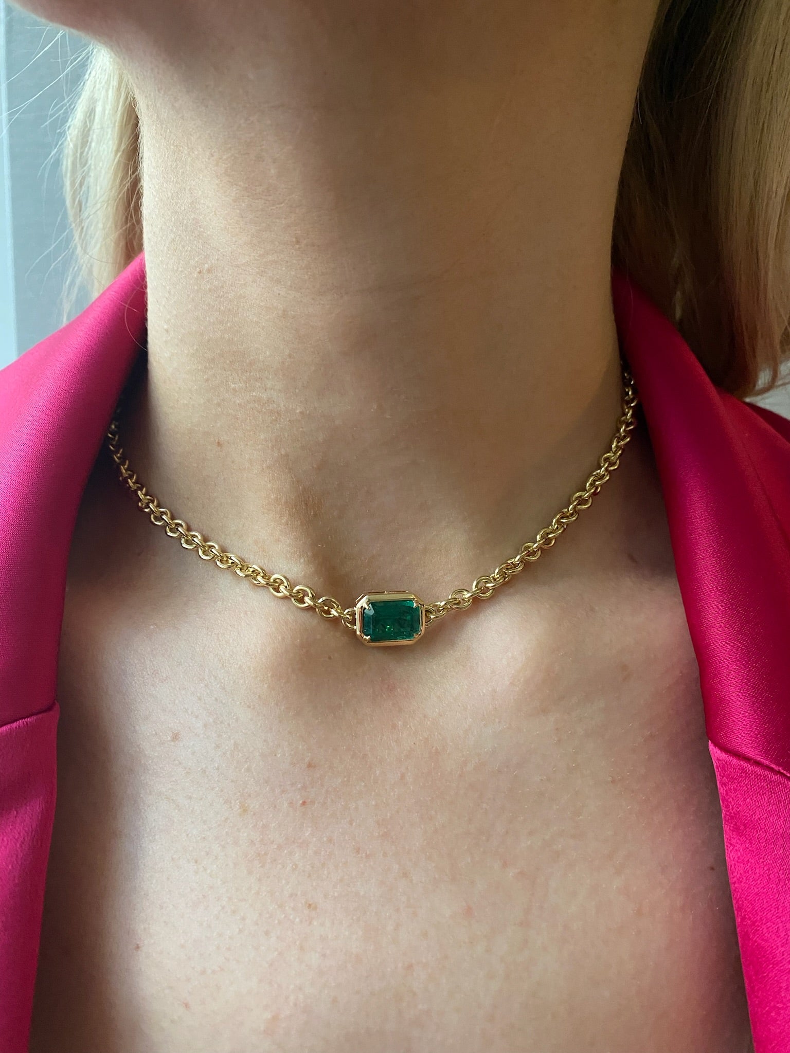 A person wears the Chunky Chain Necklace in Yellow Gold with Emerald Cut Emerald, styled with a bright pink blazer.