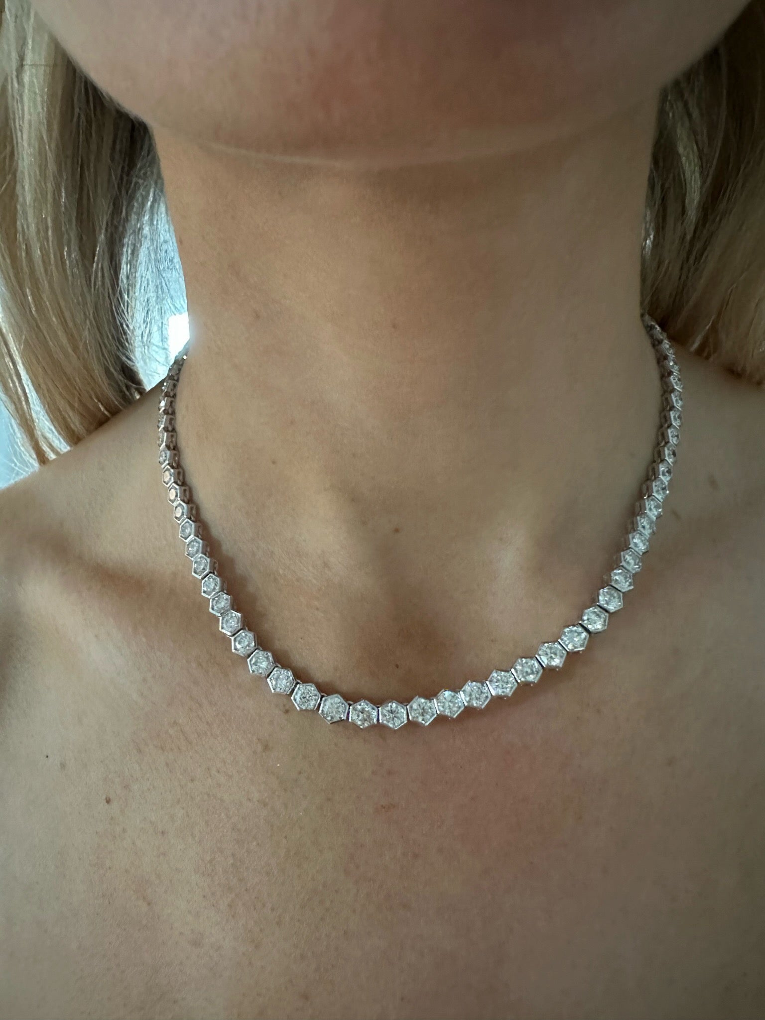 A close-up of a woman's neck wearing the Large Hexagon Bezel Set Diamond Tennis Necklace in White Gold, featuring sparkling hexagon diamonds set in 18K white gold against bare skin and collarbones.