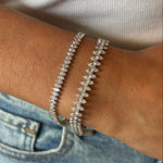 Close-up of a wrist wearing the North-South Set Diamond Marquise Tennis Bracelet in White Gold beside another sparkling piece, with a white ribbed top and blue denim jeans in the background.