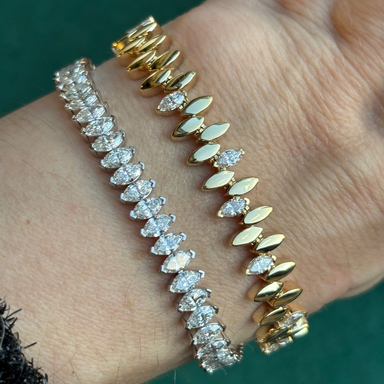 A wrist displays the Alternating Diamond Marquise Tennis Bracelet in Yellow Gold, sparkling with round SI diamonds and gold marquise shapes, set against a green background.