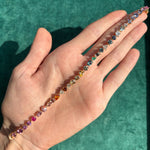 A hand with an open palm displays the Mixed Shape Multicolor Sapphire and Diamond Tennis Bracelet in yellow gold against a green textured background.