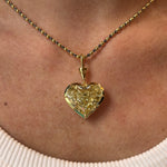 A close-up of a person wearing the Collet Set Heart Shape Fancy Yellow Diamond Necklace in Yellow Gold, featuring an 18k yellow gold chain and a heart-shaped yellow diamond pendant, against their skin and a ribbed white top.
