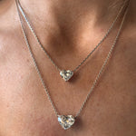 A close-up of a person’s neck wearing two layered Heart-Shaped Diamond Solitaire Pendant necklaces, each featuring a sparkling heart-shaped diamond, with one pendant resting above the other.