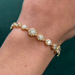 A close-up of a wrist wearing the Collet Set Round Diamond Graduated Tennis Bracelet in Yellow Gold, featuring shimmering round diamonds, against a dark green background.