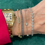 A wrist adorned with a gold Cartier watch, two gold bracelets—including the Serpentine Station Bracelet with Hexagon Bezel Set Diamonds—and a silver hexagon bracelet rests on green, with the wearer in a red sleeve.