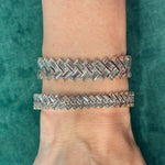 A close-up of a wrist wearing two Half-Bezel Set Chevron Diamond Tennis Bracelets in White Gold, displayed against a green textured background.