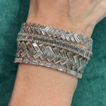 A close-up of a wrist wearing three Half-Bezel Set Chevron Diamond Tennis Bracelets in white gold, each with baguette diamonds in geometric zigzag patterns, set against a textured green fabric background.