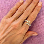 A hand with light pink manicured nails rests on lavender knit fabric, adorned with the Graduated Round Diamond Wraparound Ring in White Gold, sparkling with beautiful G-H color round diamonds on the ring finger.
