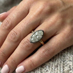 A hand with light pink manicured nails rests on knitted fabric, wearing the Collet Set Marquise Diamond Solitaire Ring in Black Rhodium and Yellow Gold, its marquise diamond beautifully catching the light.