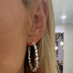 Close-up of a person with long blonde hair wearing the Mixed Shape Diamond Hoops, featuring dazzling diamonds in various shapes. The indoor background has blurred lights and a mirror.