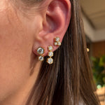 Close-up of a woman's ear adorned with Hexagon Bezel Set Round Diamond Trio Studs in 18k gold. Each earring features three bezel-set round diamonds in hexagonal shapes clustered along the earlobe, with brown hair partially visible.