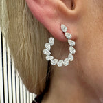 A close-up of a woman's ear adorned with the Teardrop Front-to-Back Earrings, crafted from SI1-SI2 diamonds in a curved 18k white gold setting that shimmers beautifully against her light blonde hair and fair skin.