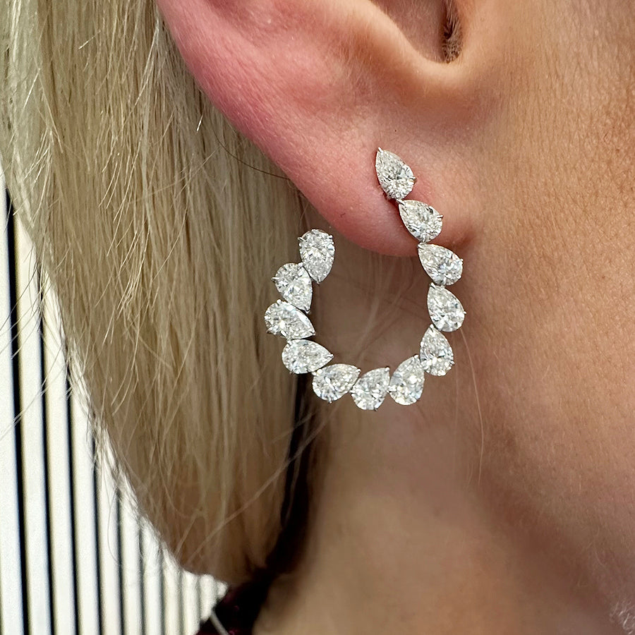A close-up of a woman's ear adorned with the Teardrop Front-to-Back Earrings, crafted from SI1-SI2 diamonds in a curved 18k white gold setting that shimmers beautifully against her light blonde hair and fair skin.