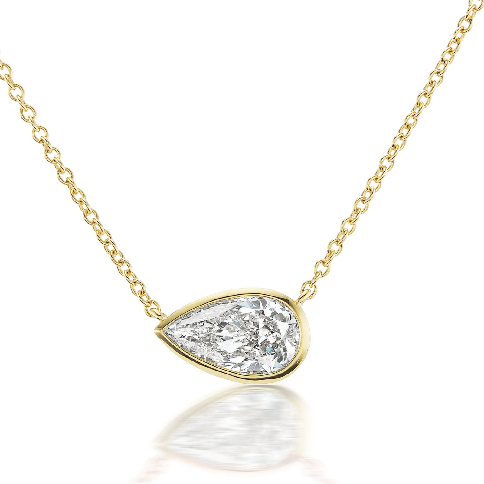 The East-West Bezel Set Pear Diamond Pendant in Yellow Gold is shown on a white background with a soft reflection below, highlighting its elegant 18K yellow gold chain (16 inches) and pear-shaped diamond pendant set in a simple bezel.
