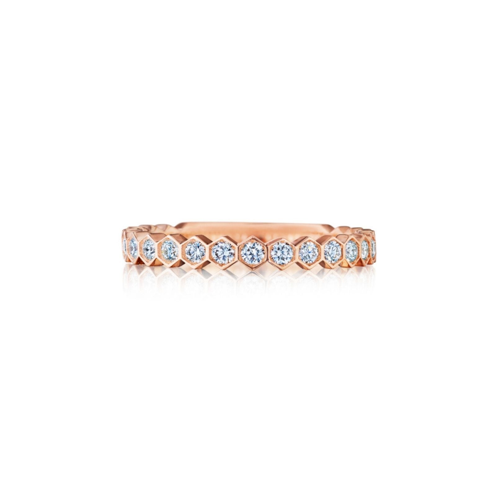 The Hexagon Bezel Set Diamond Band is an 18k rose gold eternity ring featuring round white diamonds encircling the band, all set in sleek bezel hexagons and displayed against a white background.
