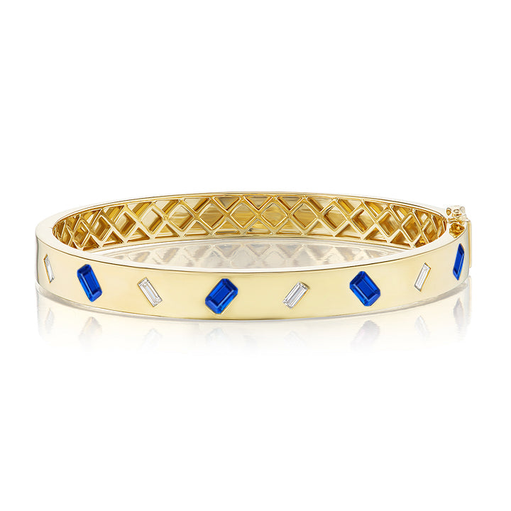 The Burnish Set Alternating Emerald Cut Diamond and Sapphire Bangle in Yellow Gold features emerald-cut diamonds and sapphires set in a geometric pattern on an 18K yellow gold band.