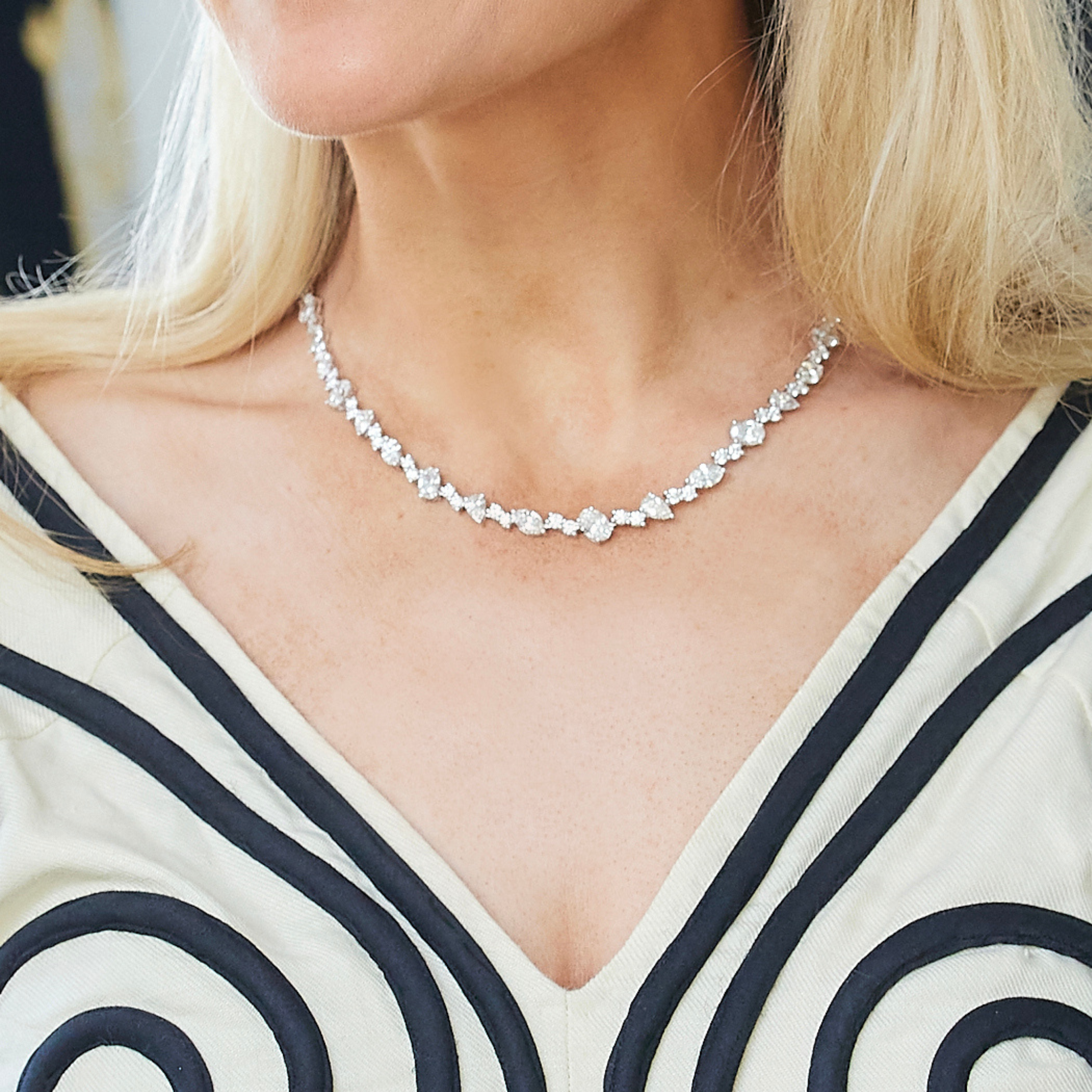 A woman in a cream dress with black swirls is shown from the shoulders up, wearing the Mixed Shape Diamond Tennis Necklace in White Gold around her neck.