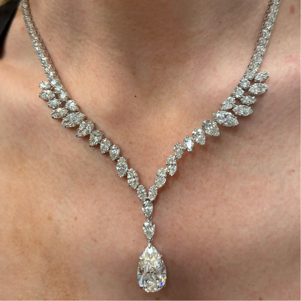A close-up of a woman's neck wearing the Mixed Shape Diamond Tennis Necklace in White Gold, adorned with a large pear-shaped pendant and rows of marquise-cut diamonds for an elegant look.