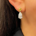 Close-up of a woman's ear adorned with Yellow Diamond & Diamond Moon Drop Earrings—18K gold drops with a yellow diamond stud and pear-shaped gemstone. She has dark hair and wears a black top.