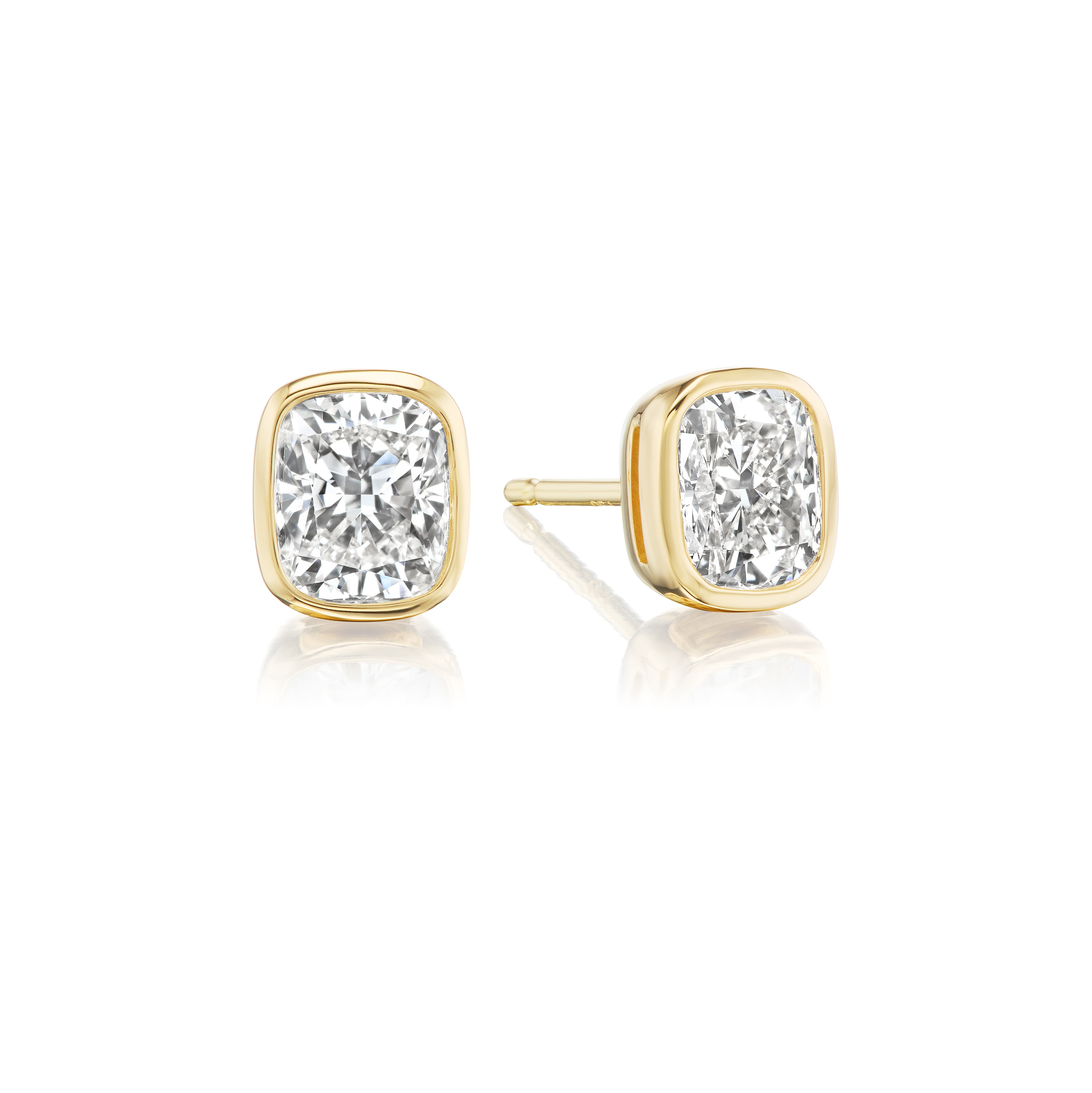 Bezel Set Cushion Cut Diamond Studs: 18K yellow gold earrings with cushion-cut, VS1 clarity diamonds in sleek bezels, shown on a white background with a subtle reflection.