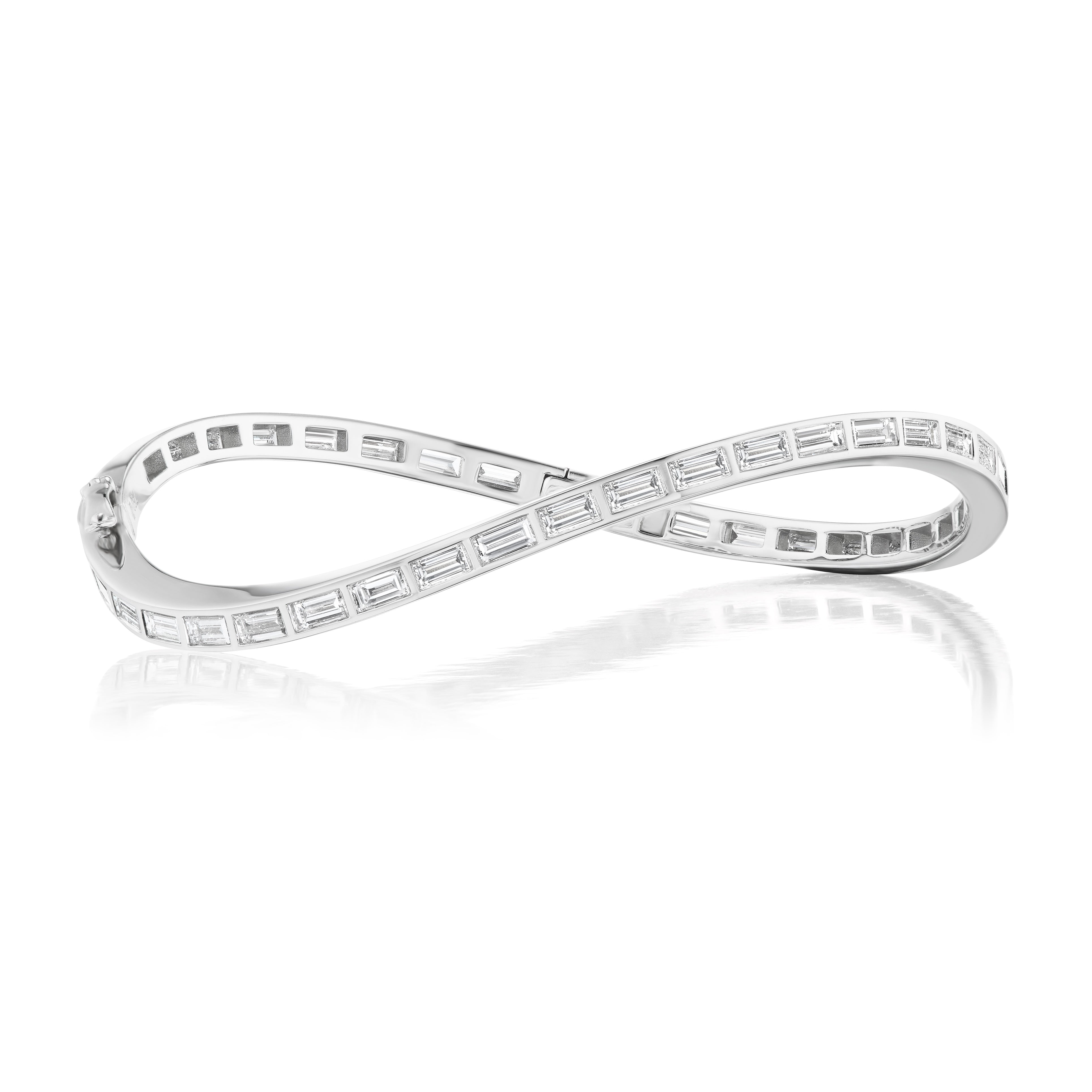 The Burnish Set Baguette Diamond Wave Bangle in White Gold, featuring baguette diamonds along its elegant curve, is displayed on a white reflective surface.