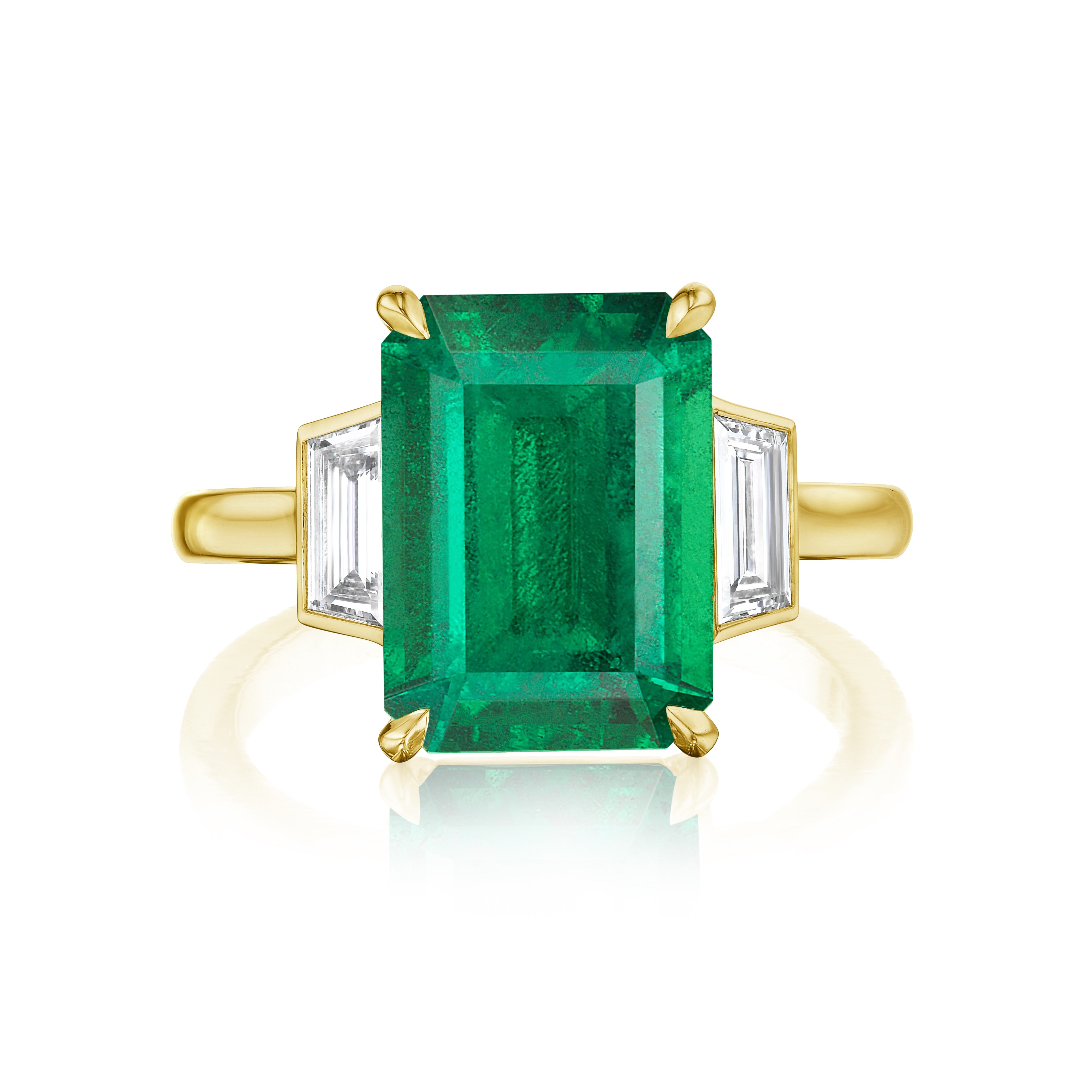 The Emerald Cut Emerald Engagement Ring features an emerald-cut center stone and bezel set diamond trapezoid side stones in 18K yellow gold, creating a stunning contrast against a white background.