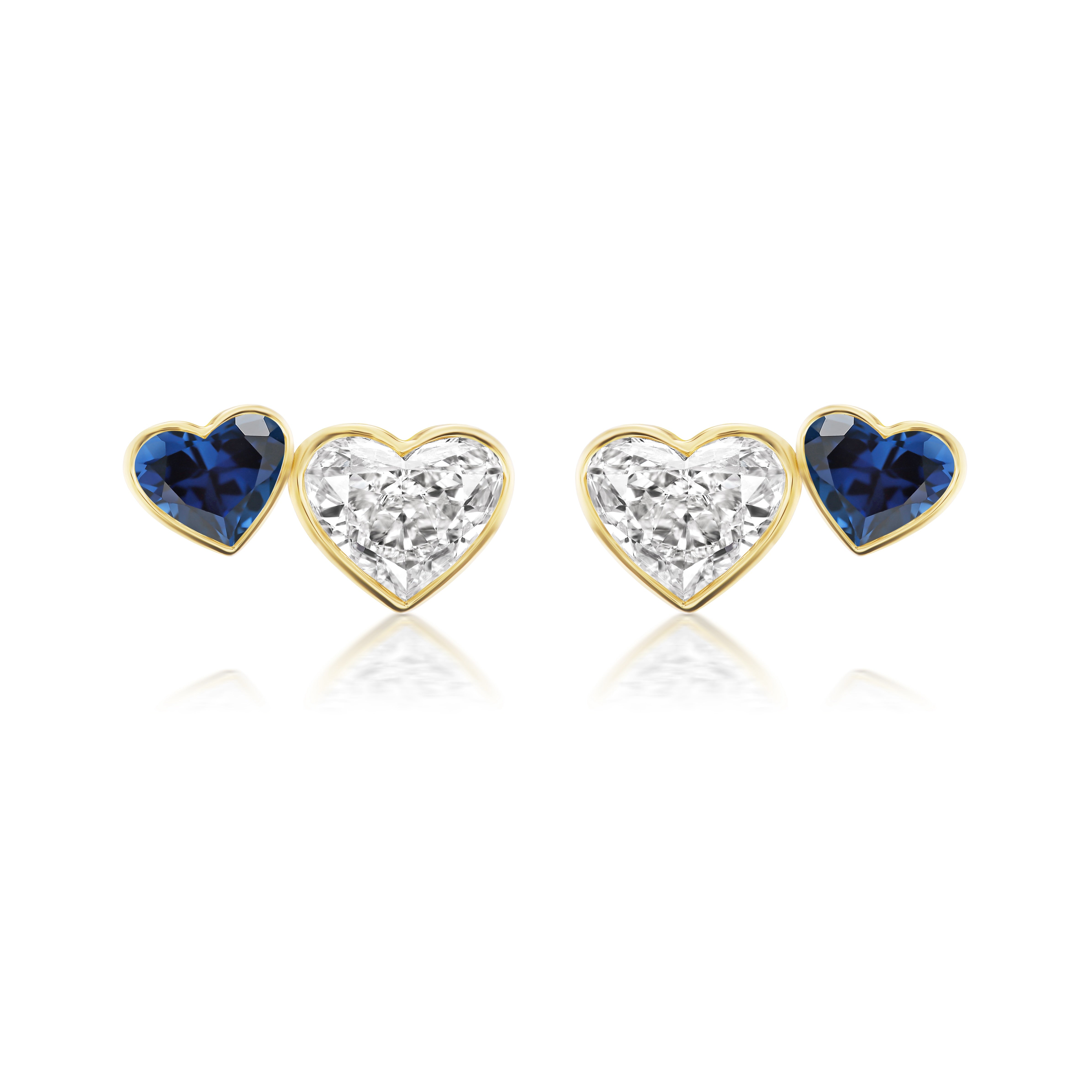 The Bezel Set Duo Studs showcase four heart-shaped earrings in yellow gold: two with diamonds and two with blue sapphires, elegantly displayed in a row on a white background.
