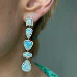 A close-up of an ear wearing the Opal and Diamond Chandelier Earrings, featuring five mixed-shape opals with pavé trim set in 18k white gold, against a neutral background.