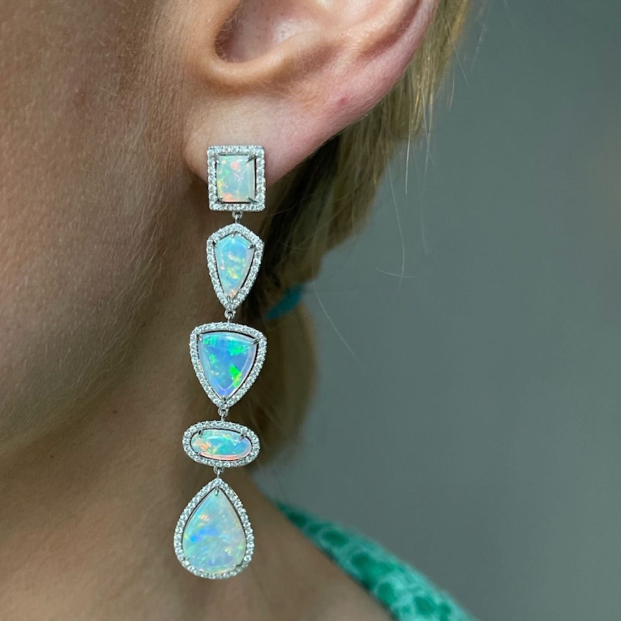 A close-up of an ear wearing the Opal and Diamond Chandelier Earrings, featuring five mixed-shape opals with pavé trim set in 18k white gold, against a neutral background.