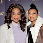 Two women with styled hair pose at an event in light-colored outfits, each wearing Art Deco Chandelier Earrings in white gold featuring emerald cut diamonds and lavender sapphires. A dark backdrop with gold text and logos is behind them.