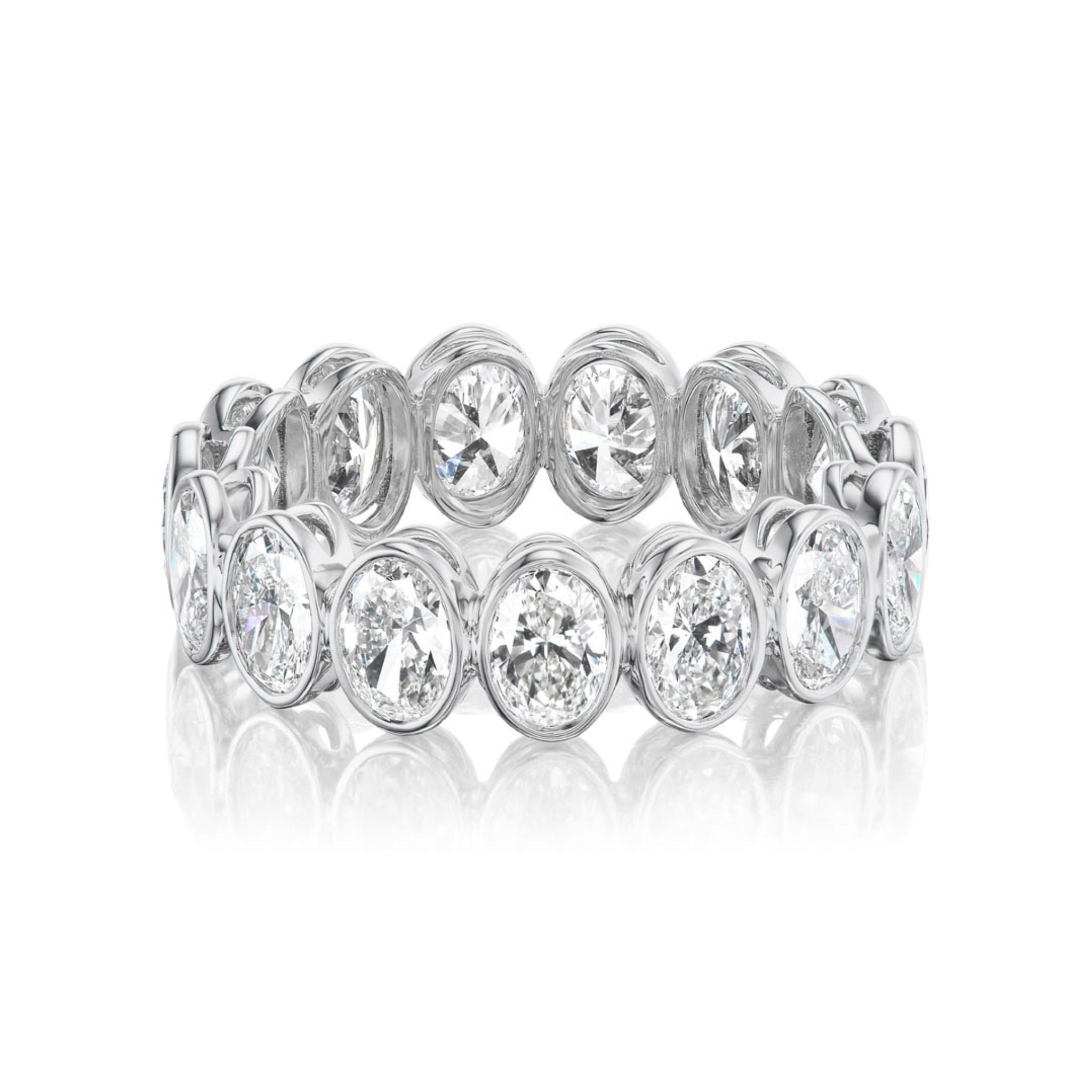 The Oval Bezel Set Diamond Eternity Band in White Gold features bezel-set oval diamonds in a continuous circle, shown on a white background with a reflection underneath.